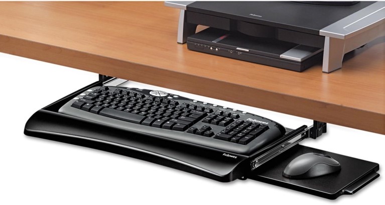 Photo of a keyboard and mouse in a pullout tray beneath a desk