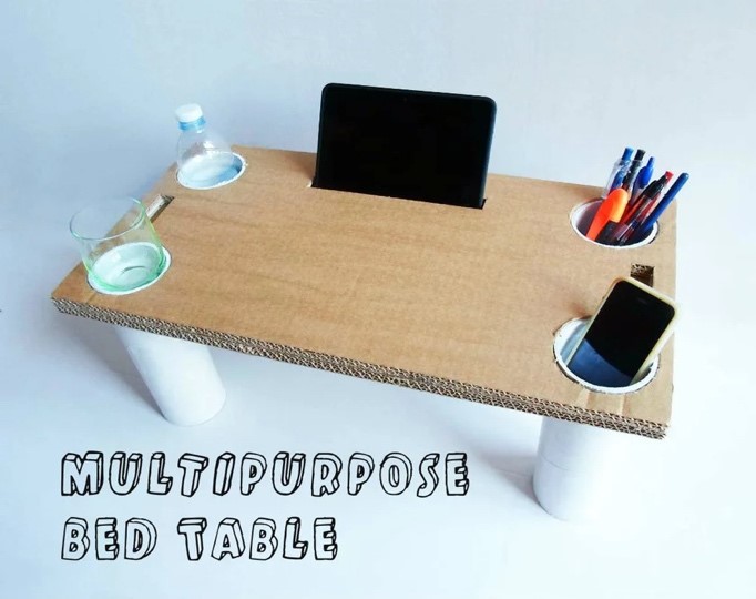 Photo of a small table made of PVC pipe and cardboard where the pipes double as legs and holders for cups, pens, phone, etc. A slot is cut near the back to hold a tablet screen upright.