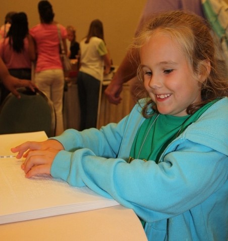 Photo of a girl reading braille with her arms spread to the sides
